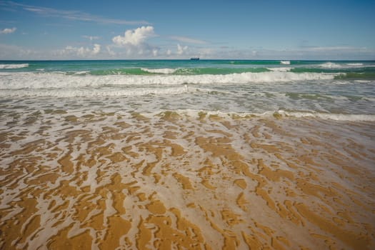 Ocean view with ship on horizon from Kawana Beach, Queensland, with surf, waves, sand and blue cloudy sky in winter.