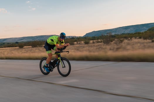 Triathlete riding his bicycle during sunset, preparing for a marathon. The warm colors of the sky provide a beautiful backdrop for his determined and focused effort