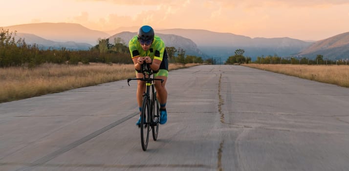 Triathlete riding his bicycle during sunset, preparing for a marathon. The warm colors of the sky provide a beautiful backdrop for his determined and focused effort