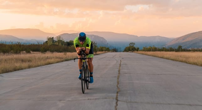 Triathlete riding his bicycle during sunset, preparing for a marathon. The warm colors of the sky provide a beautiful backdrop for his determined and focused effort