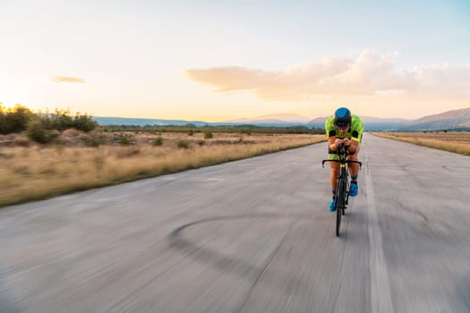 Triathlete riding his bicycle during sunset, preparing for a marathon. The warm colors of the sky provide a beautiful backdrop for his determined and focused effort