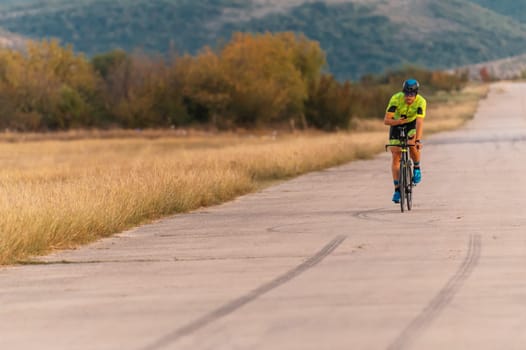 Triathlete riding his bicycle during sunset, preparing for a marathon. The warm colors of the sky provide a beautiful backdrop for his determined and focused effort