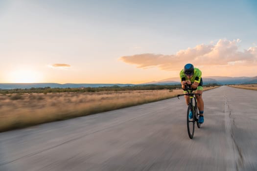 Triathlete riding his bicycle during sunset, preparing for a marathon. The warm colors of the sky provide a beautiful backdrop for his determined and focused effort