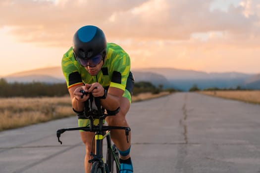 Triathlete riding his bicycle during sunset, preparing for a marathon. The warm colors of the sky provide a beautiful backdrop for his determined and focused effort