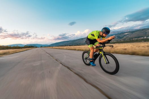 Triathlete riding his bicycle during sunset, preparing for a marathon. The warm colors of the sky provide a beautiful backdrop for his determined and focused effort
