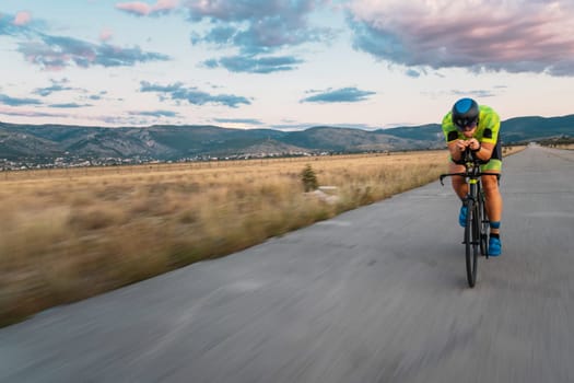 Triathlete riding his bicycle during sunset, preparing for a marathon. The warm colors of the sky provide a beautiful backdrop for his determined and focused effort