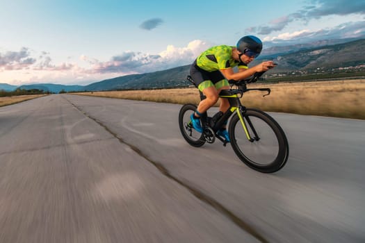Triathlete riding his bicycle during sunset, preparing for a marathon. The warm colors of the sky provide a beautiful backdrop for his determined and focused effort