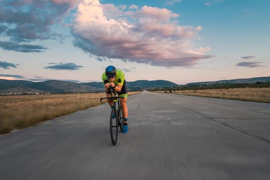 Triathlete riding his bicycle during sunset, preparing for a marathon. The warm colors of the sky provide a beautiful backdrop for his determined and focused effort