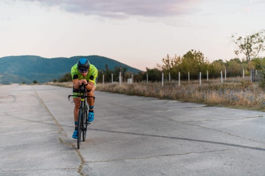 Triathlete riding his bicycle during sunset, preparing for a marathon. The warm colors of the sky provide a beautiful backdrop for his determined and focused effort