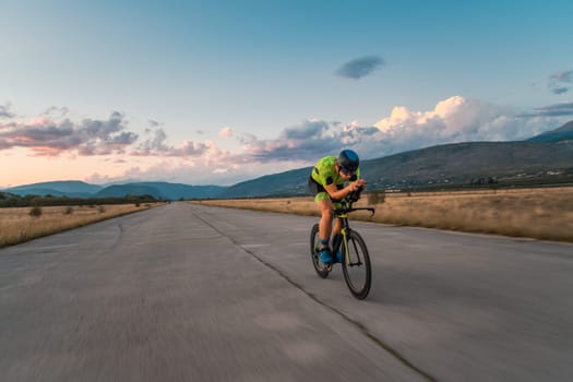 Triathlete riding his bicycle during sunset, preparing for a marathon. The warm colors of the sky provide a beautiful backdrop for his determined and focused effort