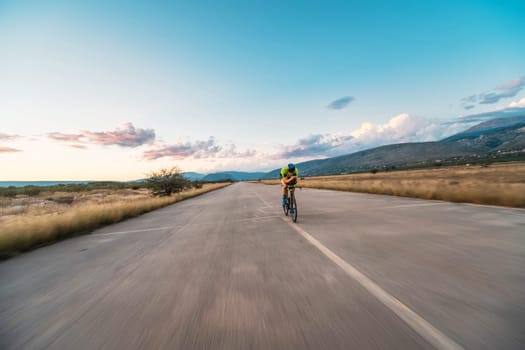 Triathlete riding his bicycle during sunset, preparing for a marathon. The warm colors of the sky provide a beautiful backdrop for his determined and focused effort