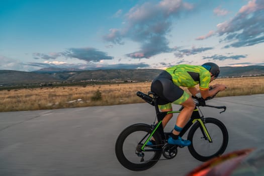 Triathlete riding his bicycle during sunset, preparing for a marathon. The warm colors of the sky provide a beautiful backdrop for his determined and focused effort