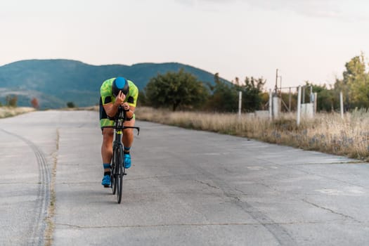 Triathlete riding his bicycle during sunset, preparing for a marathon. The warm colors of the sky provide a beautiful backdrop for his determined and focused effort
