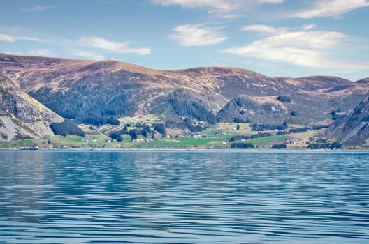 Norwegian fjord landscape. View of mountains with rugged vegetation. Crystal clear water in the foreground. Landscape from Scandinavia