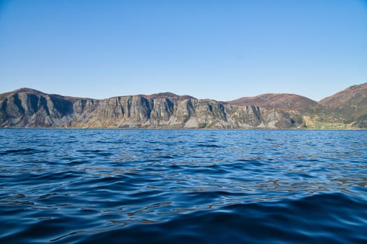 Norwegian fjord landscape. View of mountains with rugged vegetation. Crystal clear water in the foreground. Landscape from Scandinavia