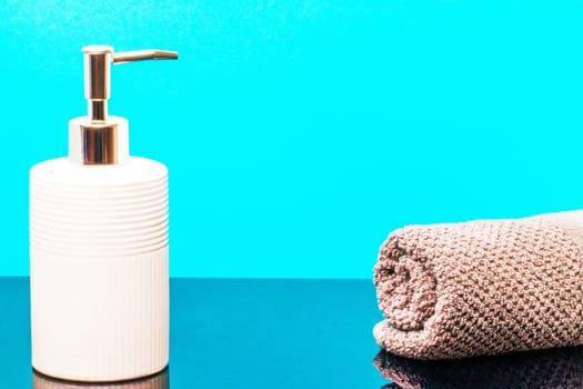 Macro of a beauty cosmetic makeup bottle and a fresh soft terry bath towel on dark table over blue background. Copy space for product display montage.