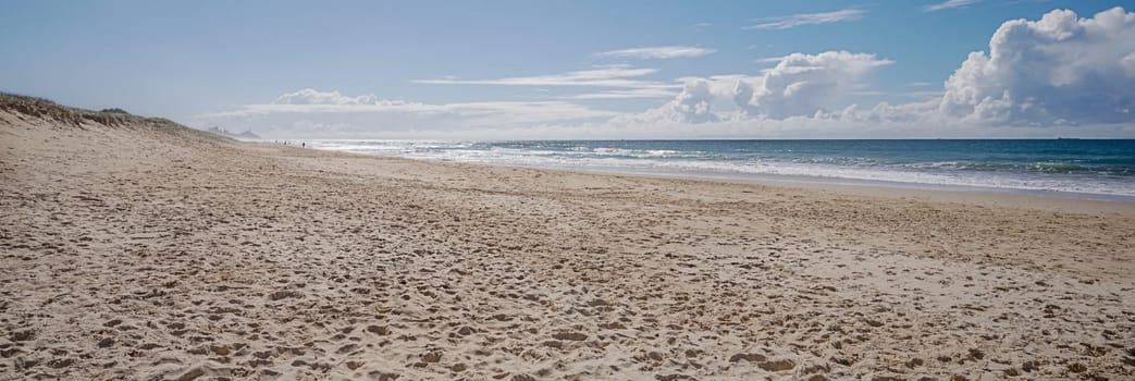 Seascape landscape panoramic view of sandy beach, ocean and straight horizon with lots of footprints in the sandy foreshore