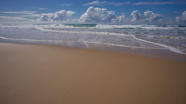 A beach scene with copy space for tourism with sand surf waves clouds blue sky in winter Queensland Australia