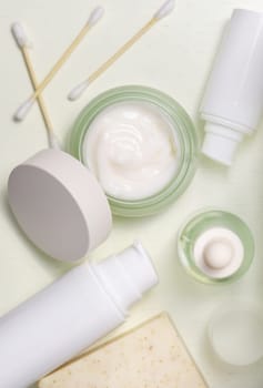 Opened cream jar with balnk lid near personal care products on light yellow top view, packaging mockup, copy space. Natural cosmetic products for woman beauty routine