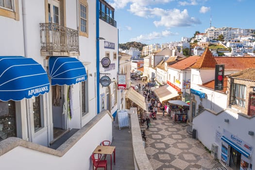 Albufeira, Portugal - April 27, 2024: traditional buildings and tourists photographed in a street of  Albufeira at the Algarve coast of Portugal