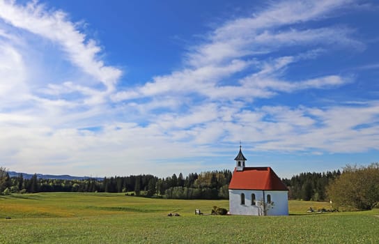 A small chapel in spring under a white-blue sky in the Allgäu