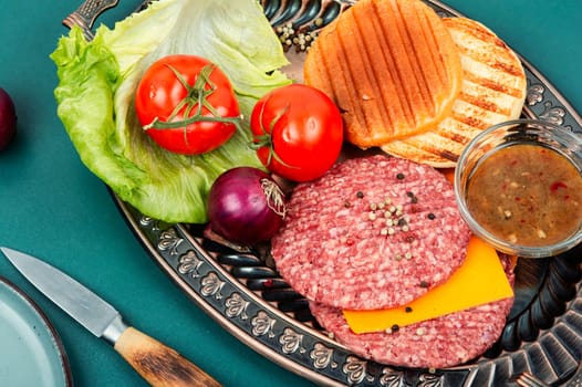 Fresh burger patties, cheese, vegetables and burger buns for preparation. Raw steak cutlets with mince meat.