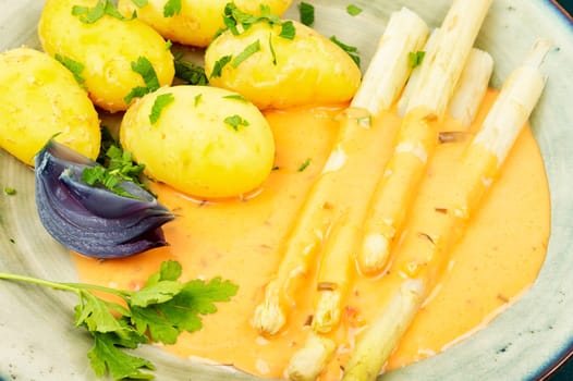 Vegan food, new boiled potatoes and white asparagus on rustic wooden table.