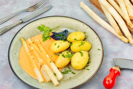 Vegan food, new boiled potatoes and white asparagus on rustic wooden table.