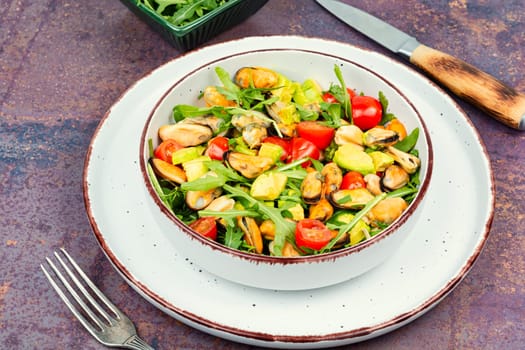 Plate with vitamin salad of mussels, arugula, tomato and avocado. Top view.