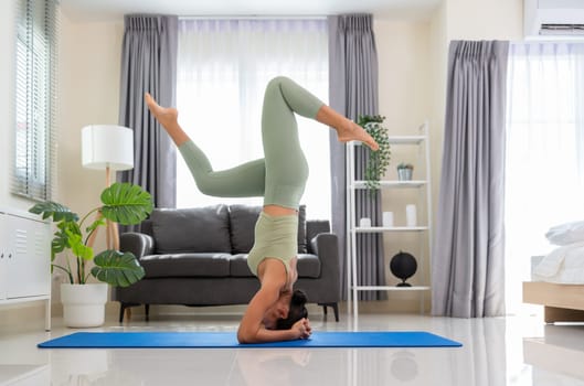 Young attractive female practicing morning yoga at home, standing in Salamba sirsasana exercise or Headstand pose on mat in bedroom. Healthy life and fitness training workout at home concept