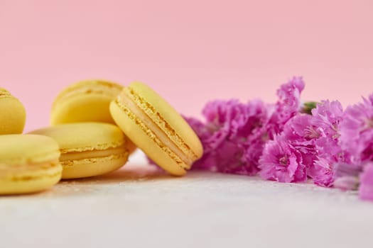 delicate yellow macarons dessert with pink flowers on pink background