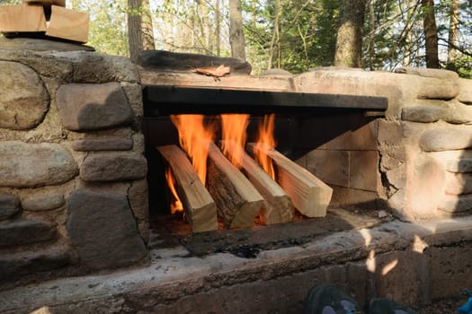 A stone outdoor fireplace with a fire burning, surrounded by trees.