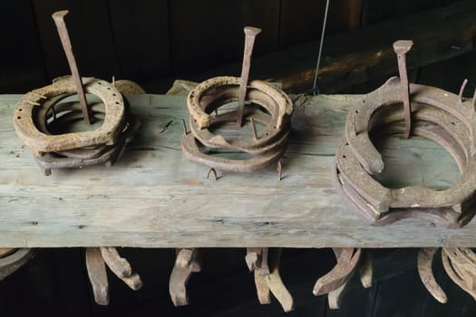 Old, rusty horseshoes stacked on a wooden beam in a rustic setting.