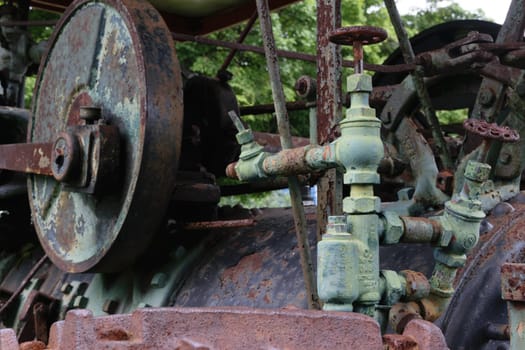 Close-up of an old, rusty industrial machine with pipes and valves, surrounded by greenery.