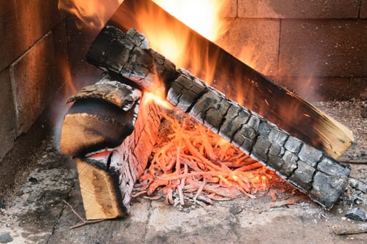 A close-up of burning firewood in a fireplace, with flames and glowing embers.