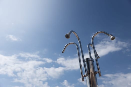 Beach Shower Heads Against Blue Sky. Group of metal shower heads standing high against a blue sky with scattered clouds. Copy space.High quality photo