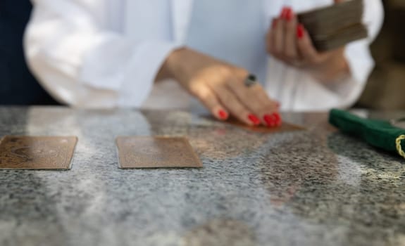 Montenegro, Budva, May 6, 2024.Woman with red nails and white blouse laying out tarot cards on granite table, green velvet bag visible.