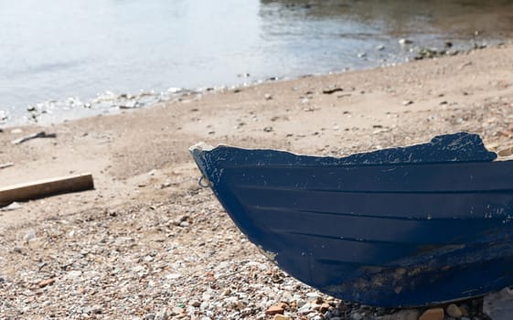 Wrecked fishing blue boat after a storm on a pebble beach with the sea in the background.