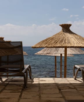 Sun loungers and thatched umbrellas are set on a stone patio overlooking the sea. vacation themes and relaxation concepts. High quality photo