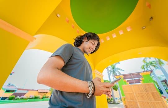 Low angle view of young man using cell phone outdoors. Smiling latin guy texting with cell phone in Nagarote park