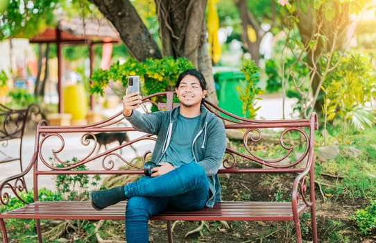 Relaxed guy taking a selfie sitting on a bench at sunset. Smiling man sitting on a bench taking a selfie in Nagarote Park