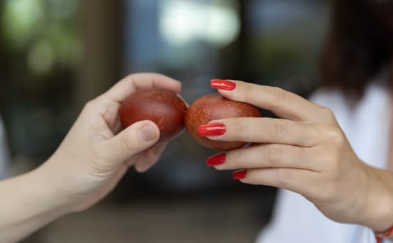 Two hands holding brown eggs for traditional Easter holiday, one hand with red nails. Blurred background with festive atmosphere. Copy space. of Easter celebration content.High quality photo