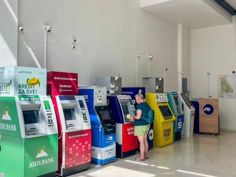 Banja Luka, Bosnia and Herzegovina, August 23, 2023: ATMs from various banks like Atos Bank, UniCredit, Addiko, NLB, DCX Exchange, Sparkasse, Cash Point. A row of ATMs in a shopping mall. Woman withdrawing money from an ATM