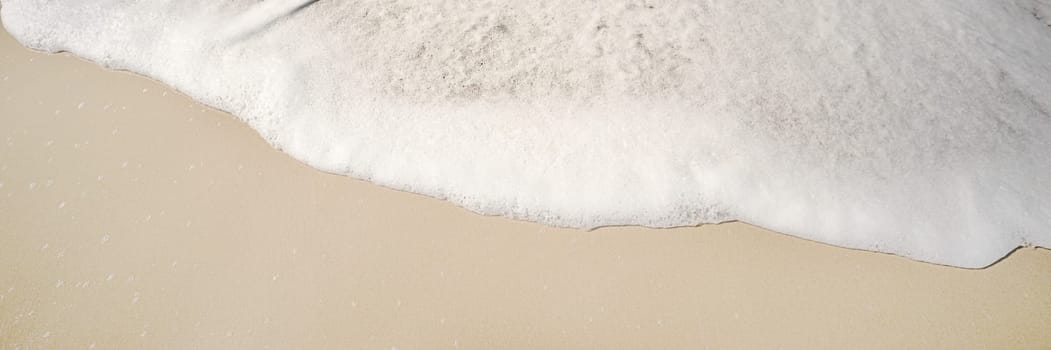 White fluffy foam from a wave breaking rolling onto the sandy beach background image
