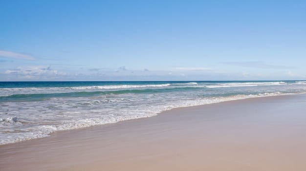 Panoramic beach scene with wet smooth sand, sea, breaking waves, horizon and blue sky and copyspace, blank space with no landmarks, nobody, no people