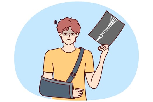 Man injured arm and shows picture of bone with traces of fracture taken by doctor using X-ray machine. Guy injured in car accident has broken arm and needs treatment or rehabilitation