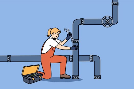Woman plumber repairs pipes in factory, using wrench to fix crack in industrial pipeline. Girl in overalls works as plumber, easily doing men job and enjoying difficult profession.