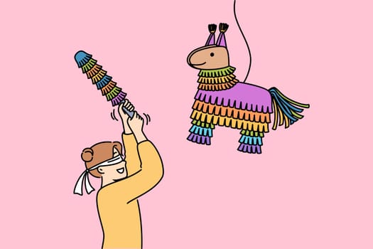 Little girl hits horse-shaped pinata filled with candies and sweets during birthday party. Traditional mexican pinata for happy blindfolded child and children activities organization
