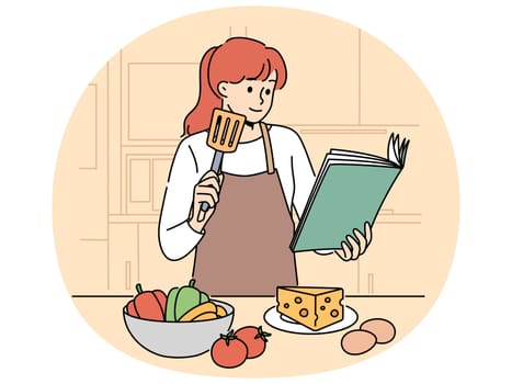 Woman with cookbook is standing in kitchen wanting to cook delicious dinner and vegetables and cheese with eggs. Girl cook in apron uses cookbook while preparing salad or appetizers
