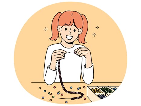 Little girl weaves beaded jewelry sitting at table and creating handmade necklace or bracelet. Elementary school girl with creative hobby creates jewelry and wants to be designer when grows up.